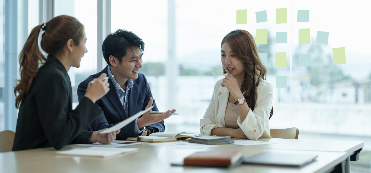 Three people sitting at a table with documents and sticky notes in an office setting